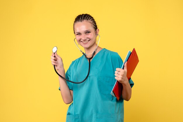 Vista frontal de la doctora en traje médico con estetoscopio y análisis en pared amarilla