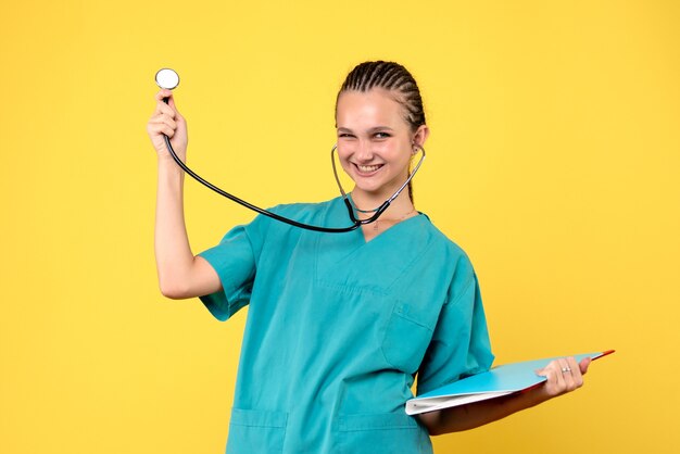 Vista frontal de la doctora en traje médico con estetoscopio y análisis en pared amarilla