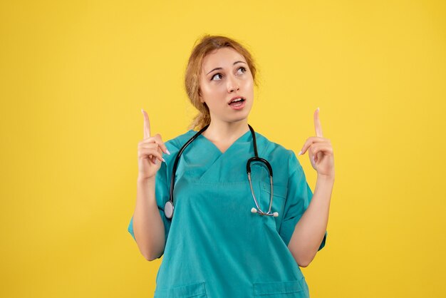 Vista frontal de la doctora en traje médico con estetoscopio en pared amarilla