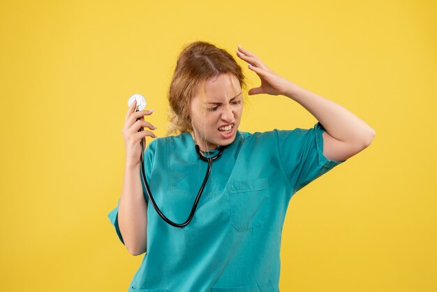 Vista frontal de la doctora en traje médico con estetoscopio en pared amarilla