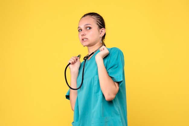 Vista frontal de la doctora en traje médico con estetoscopio en pared amarilla