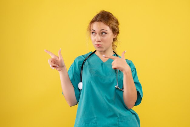 Vista frontal de la doctora en traje médico con estetoscopio en pared amarilla