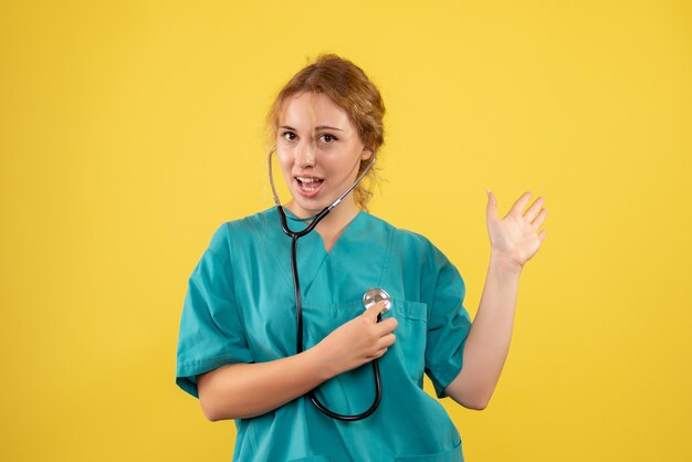 Vista frontal de la doctora en traje médico con estetoscopio en pared amarilla