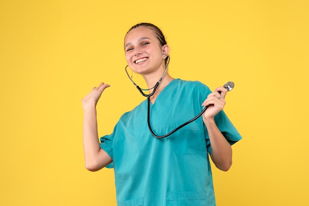 Vista frontal de la doctora en traje médico con estetoscopio en pared amarilla