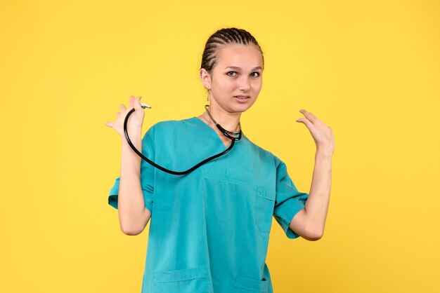 Vista frontal de la doctora en traje médico con estetoscopio en pared amarilla