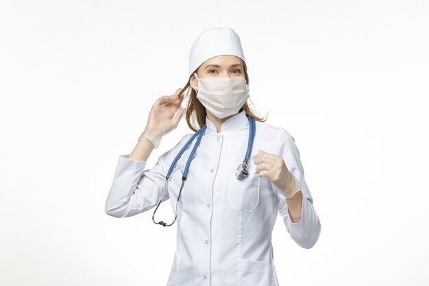 Vista frontal doctora en traje médico con máscara debido al coronavirus en la pared blanca enfermedad covid del virus pandémico