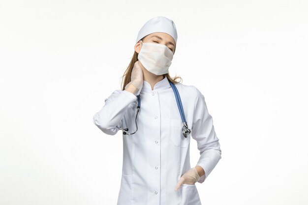 Vista frontal doctora en traje médico con máscara debido a coronavirus que sufre de dolor de cuello en la pared blanca enfermedad virus covid-enfermedad pandémica