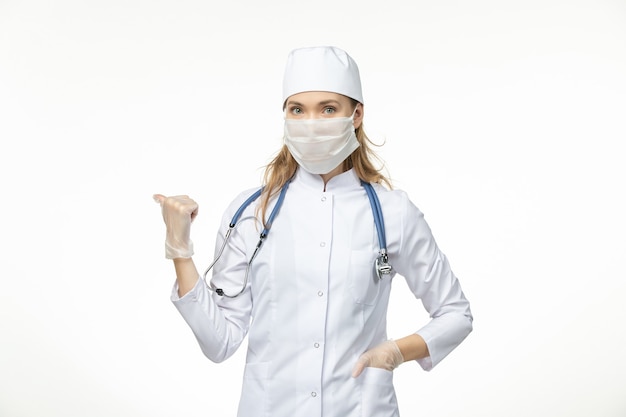 Vista frontal doctora en traje médico con máscara estéril debido a coronavirus en la pared blanca enfermedad enfermedad pandémica covid-