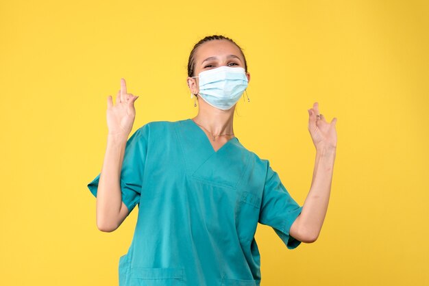 Vista frontal de la doctora en traje médico y máscara estéril en una pared amarilla