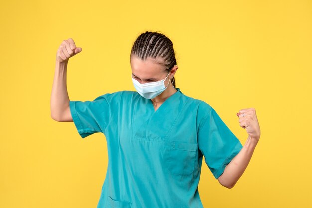 Vista frontal de la doctora en traje médico y máscara estéril en una pared amarilla