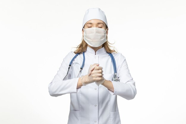 Vista frontal doctora en traje médico con máscara y guantes debido al coronavirus en el covid-virus pandémico de la enfermedad de la pared blanca