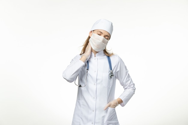 Vista frontal doctora en traje médico con máscara con guantes debido al coronavirus en la pared blanca clara enfermedad covid-virus pandémico