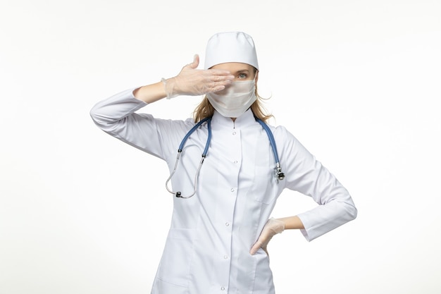 Vista frontal doctora en traje médico con máscara y guantes debido al coronavirus en la pared blanca enfermedad virus covid-enfermedad pandémica
