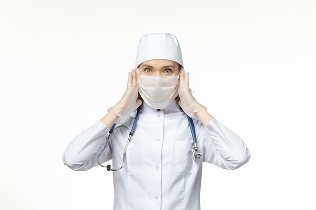 Vista frontal doctora en traje médico con máscara y guantes debido al coronavirus en la pared de luz enfermedad por virus de la enfermedad pandémica covid