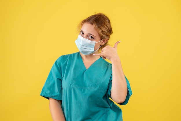 Vista frontal de la doctora en traje médico y máscara en la pared amarilla