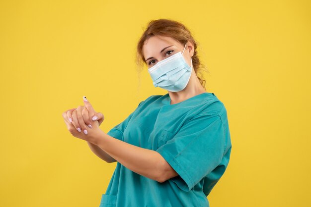 Vista frontal de la doctora en traje médico y máscara en la pared amarilla