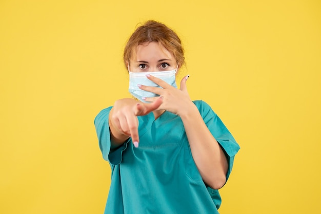 Vista frontal de la doctora en traje médico y máscara en la pared amarilla