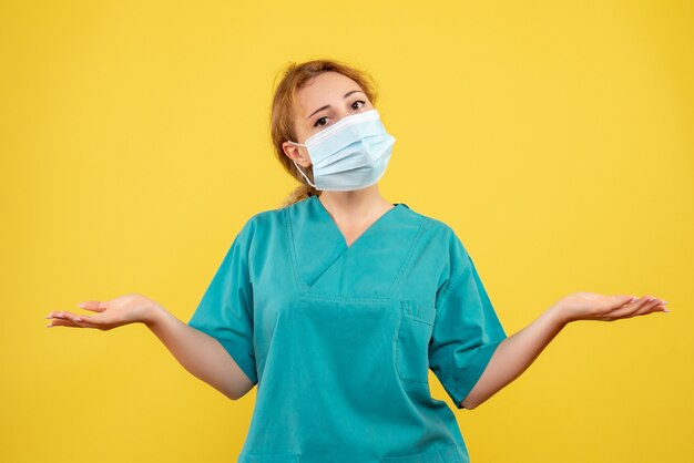 Vista frontal de la doctora en traje médico y máscara en la pared amarilla