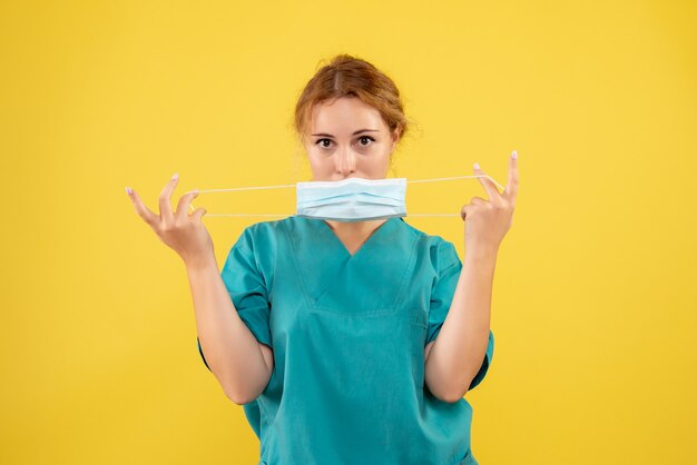 Vista frontal de la doctora en traje médico y máscara en la pared amarilla