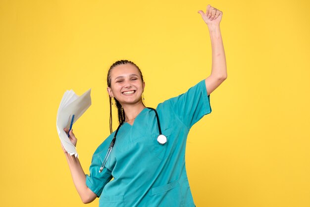 Vista frontal de la doctora en traje médico con papeles en la pared amarilla