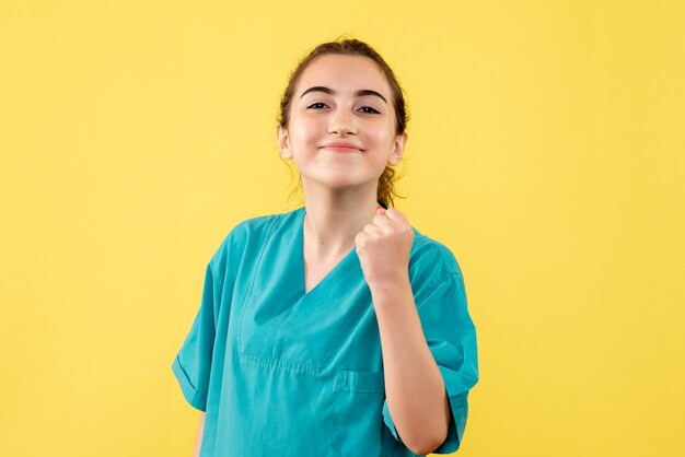 Vista frontal de la doctora en traje médico en pared amarilla