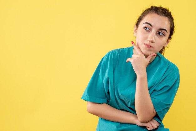 Vista frontal de la doctora en traje médico en pared amarilla