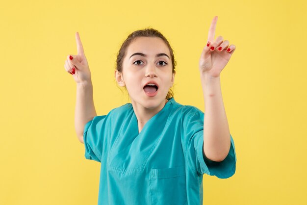 Vista frontal de la doctora en traje médico en pared amarilla