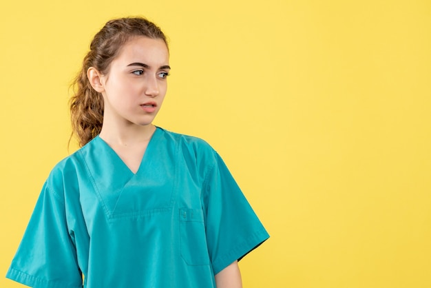Vista frontal de la doctora en traje médico en pared amarilla