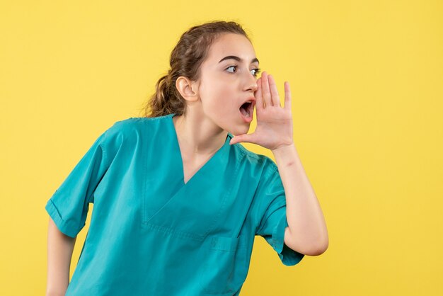 Vista frontal de la doctora en traje médico en pared amarilla