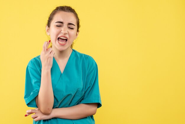 Vista frontal de la doctora en traje médico en pared amarilla