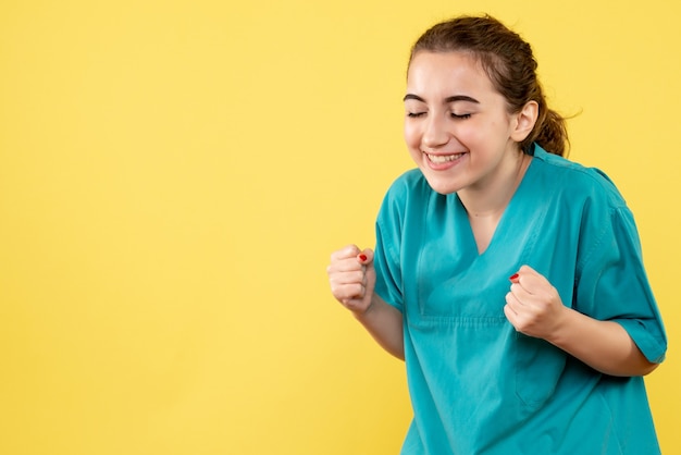 Vista frontal de la doctora en traje médico regocijándose en la pared amarilla