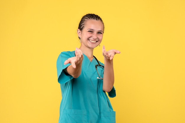 Vista frontal de la doctora en traje médico riendo en la pared amarilla