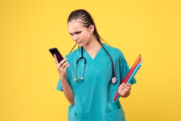 Vista frontal de la doctora en traje médico sosteniendo el teléfono en la pared amarilla