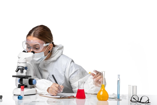 Vista frontal doctora en traje de protección y con máscara escribiendo notas sobre fondo blanco claro medicina covid-salud pandemia virus