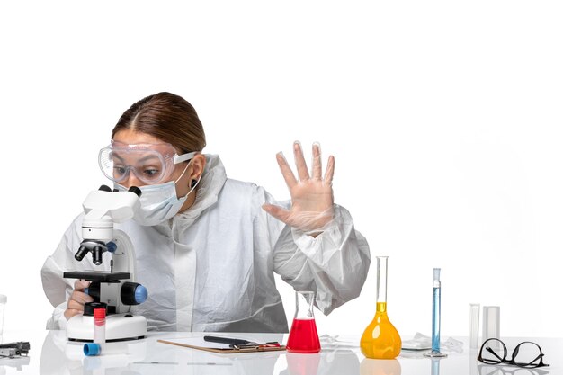 Vista frontal de la doctora en traje de protección y con máscara con microscopio sobre fondo blanco medicina covid- virus de la pandemia de salud