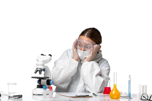 Vista frontal doctora en traje protector y con máscara mirando microscopio sobre fondo blanco virus covid salud pandémica coronavirus