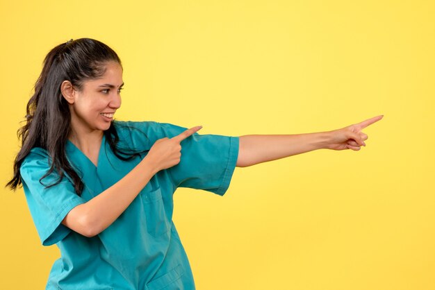 Vista frontal de la doctora en uniforme apuntando en la dirección correcta en la pared amarilla