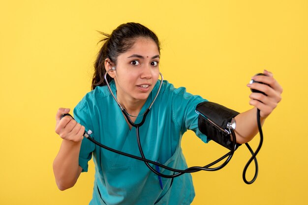 Vista frontal de la doctora en uniforme sosteniendo el dispositivo de medición de la presión arterial