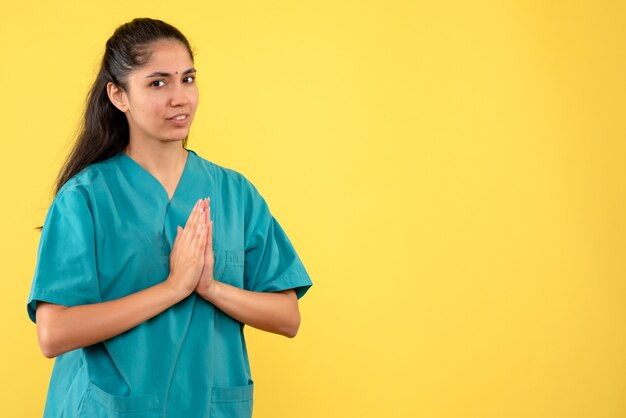 Vista frontal doctora en uniforme uniendo las manos juntas de pie