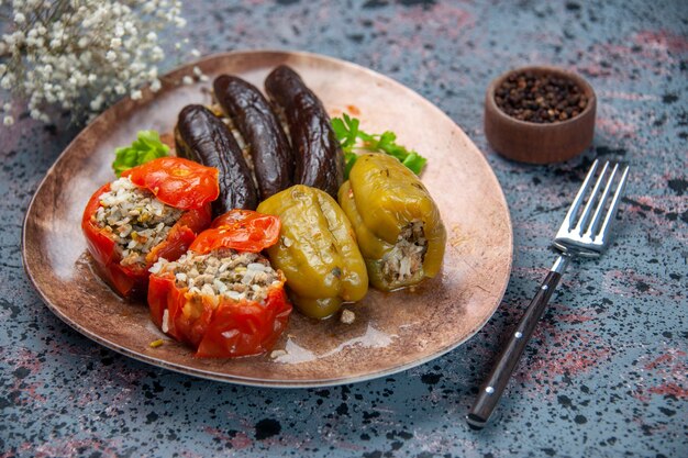 Vista frontal dolma de berenjena con tomates cocidos y pimientos rellenos de carne molida dentro de la placa sobre fondo azul plato de comida color cena comida