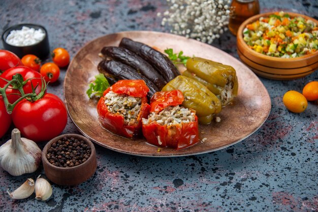 Vista frontal dolma berenjena con tomates cocidos y pimientos rellenos con carne molida dentro de la placa sobre fondo azul.