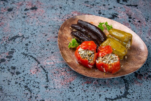 Vista frontal dolma berenjena con tomates cocidos y pimientos rellenos con carne molida dentro de la placa sobre fondo azul.