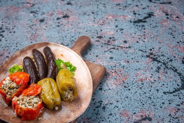 Vista frontal dolma de berenjena con tomates cocidos y pimientos rellenos de carne molida sobre fondo azul.