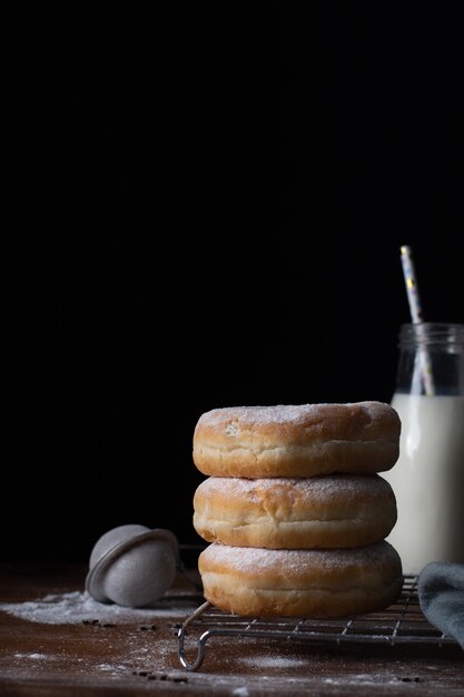 Vista frontal de donas apiladas con azúcar en polvo y botella de leche