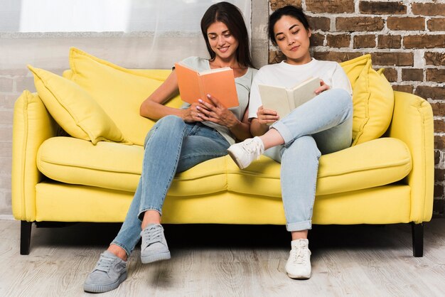 Vista frontal de dos amigos relajándose en casa en el sofá con libros