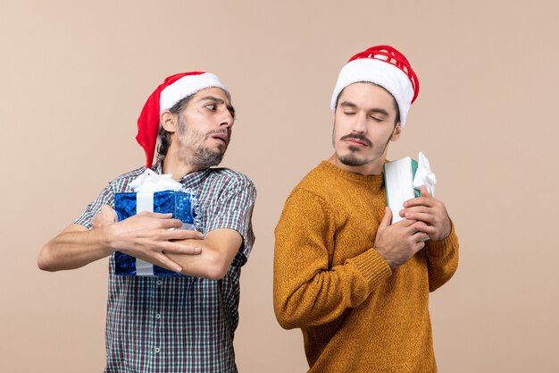 Vista frontal de dos chicos confundidos con gorro de Papá Noel y sosteniendo apretados sus regalos sobre fondo beige aislado