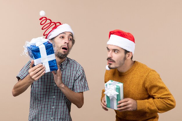 Vista frontal de dos chicos confundidos con gorro de Papá Noel y sosteniendo sus regalos sobre fondo aislado