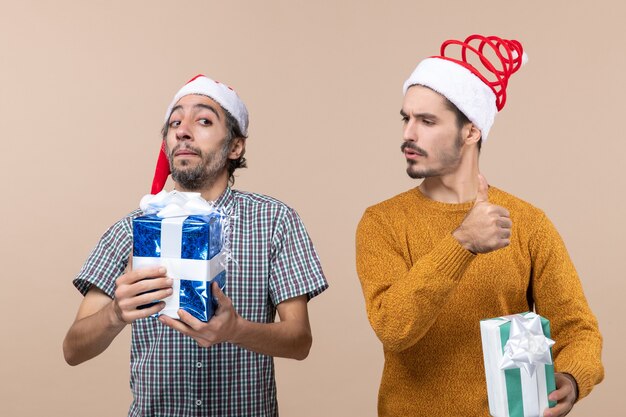 Vista frontal de dos chicos contentos con gorro de Papá Noel y sosteniendo regalos de Navidad