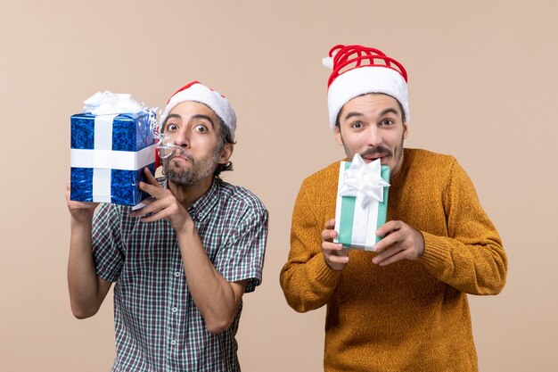 Vista frontal de dos chicos encantados con gorro de Papá Noel y sosteniendo regalos sobre fondo aislado