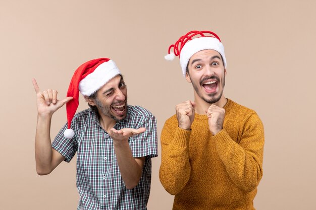 Vista frontal de dos chicos felices con gorro de Papá Noel, uno con el ojo parpadeado y el otro con puño de golpe sobre fondo beige aislado